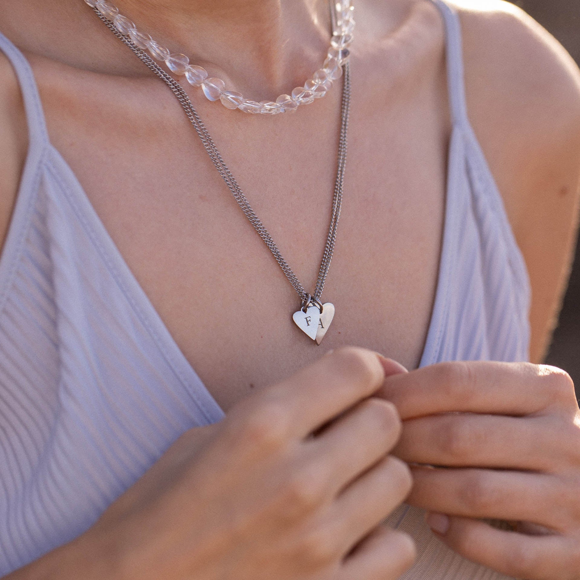 Silberne Herz-Halskette mit Initialen, getragen über einem blauen Top, von PURELEI.