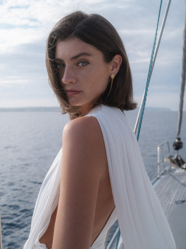 PURELEI Allure Ohrringe aus 14K Gold, organisch geformt mit filigranen Ketten, elegant am Segelboot vor Meeressilhouette