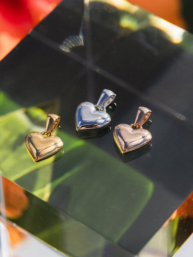 PURELEI Aloha Love Charm Herzanhänger in Gold, Silber und Roségold, clean & elegant auf Glasplatte inszeniert.