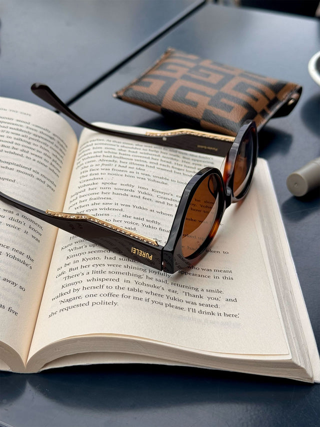 Lagoon Sonnenbrille aus dunkelbraunem Acetat mit goldener Verzierung, ovaler Rahmenform, PURELEI, elegant und modern.
